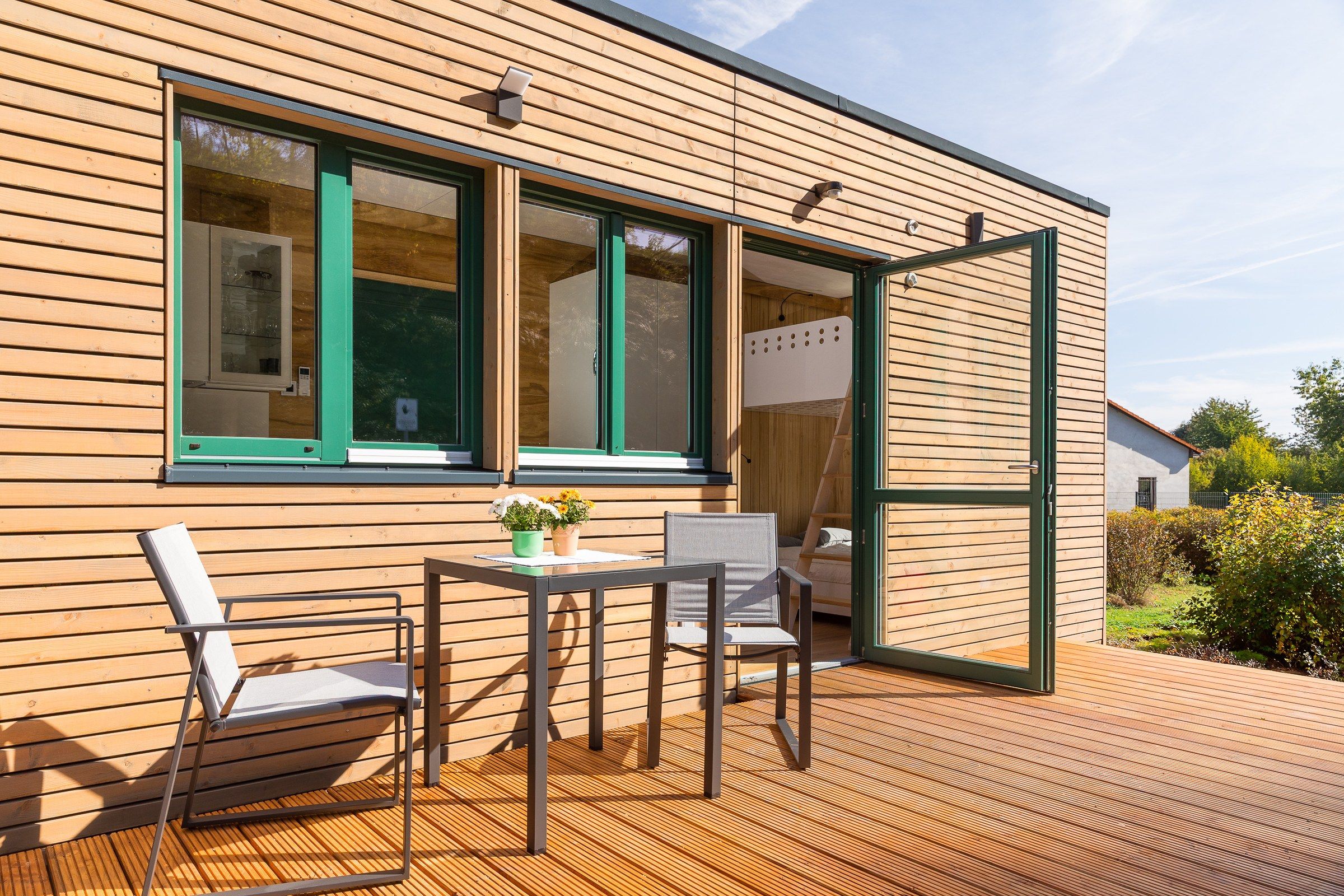 Terrasse eines rethink Tiny House mit Holzfassade, Tisch und Stühlen vor der geöffneten Glastür